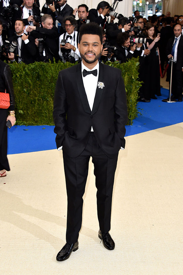 The Weeknd walked the red carpet in a classic Valentino black suit and  bowtie. He added an oversize flower brooch as a final accent – replay254